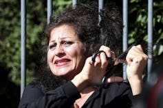 A woman wearing black cuts some of her hair with a pair of scissors.