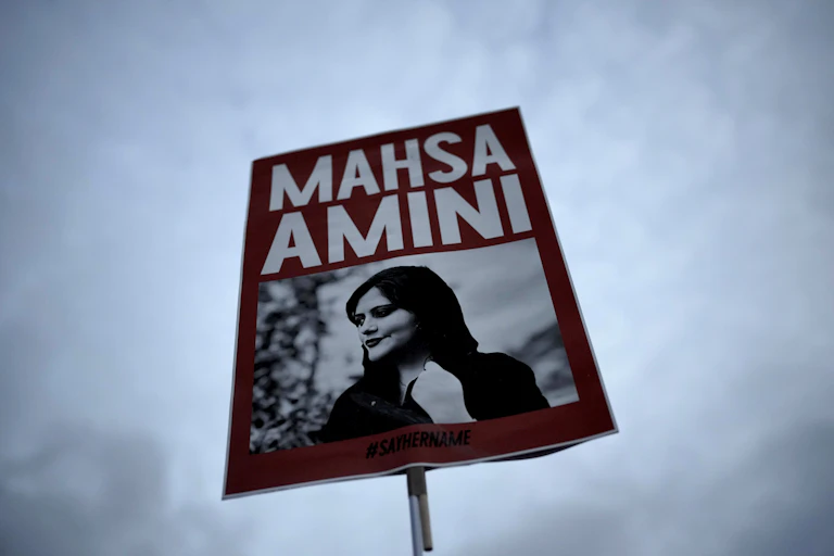 A red placard with a black and white photo of a woman with the words Mahsa Amini.