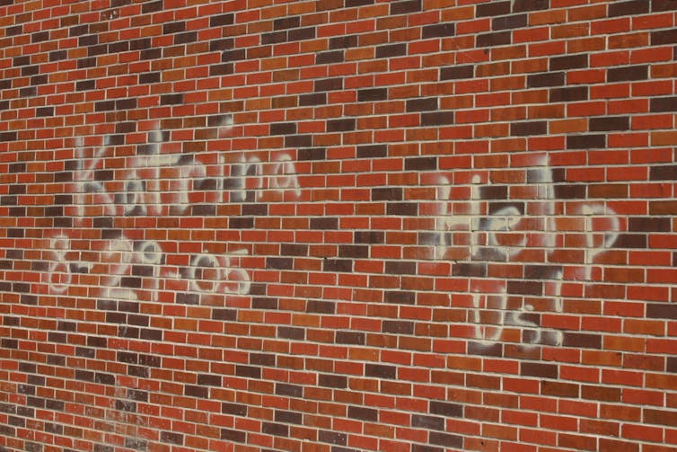 White spray paint on a brick wall states: 'Katrina 8-29-05' and 'Help Us!'