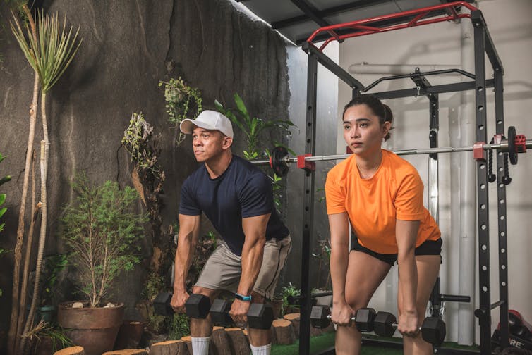 Two people do deadlifts in a gym.