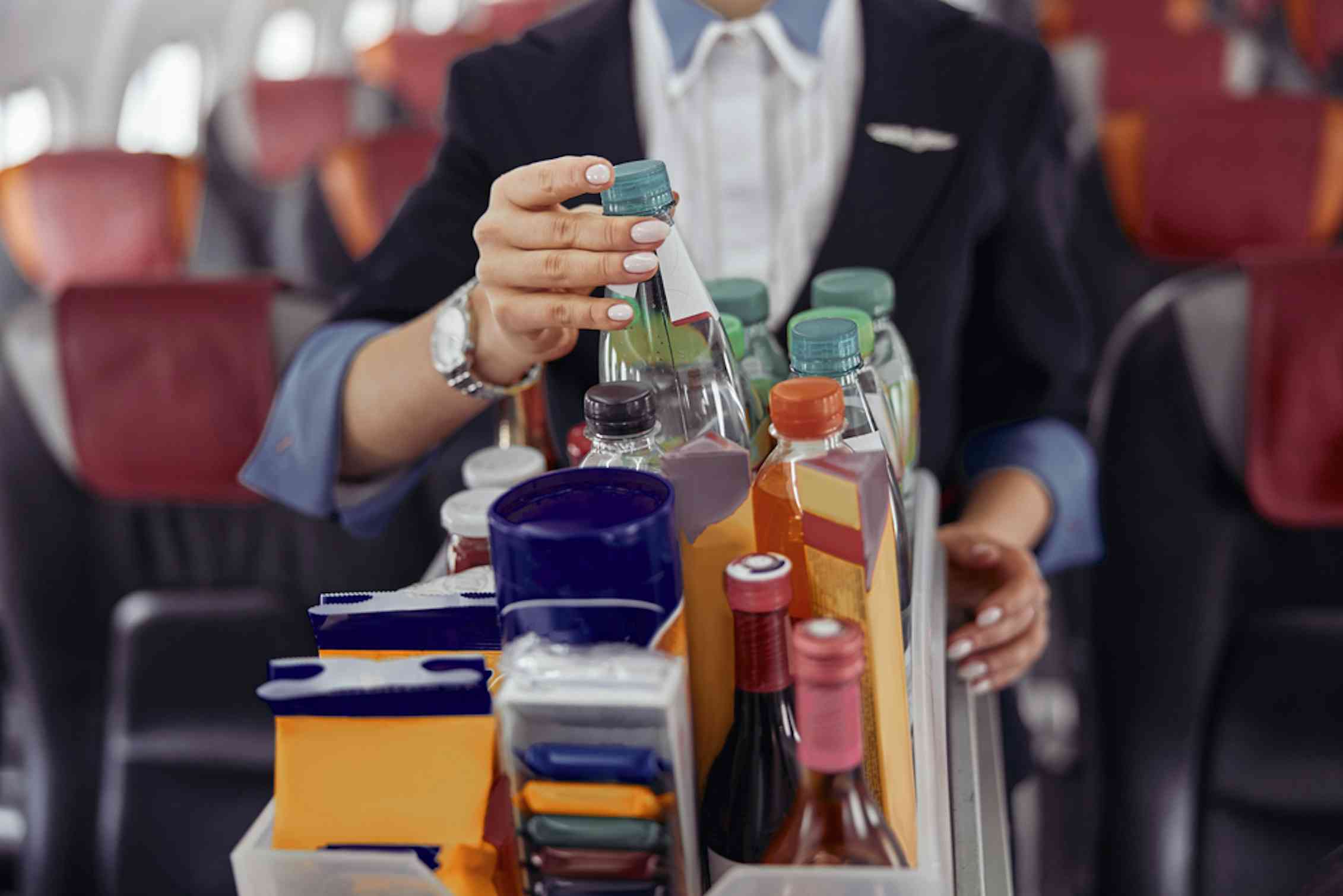 Assistente di volo che preleva una bottiglia d'acqua dal carrello delle bevande in aereo