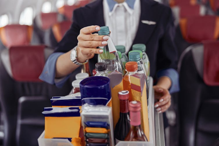 Air steward picking up bottle of water from drinks trolley on plane