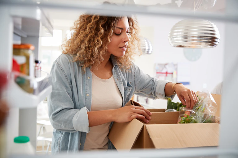 A woman sifts through bagged vegetables in a cardboard box.