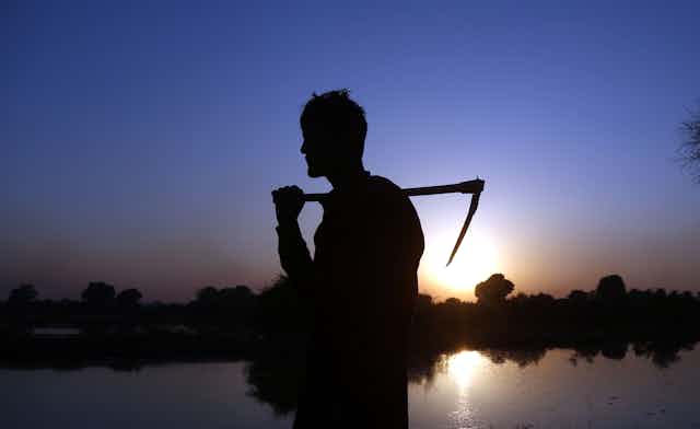 Silhouette of a man holding a scythe in front of a flooded field.