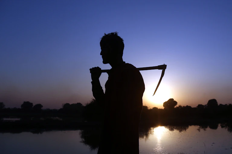 Silhouette of a man holding a scythe in front of a flooded field.