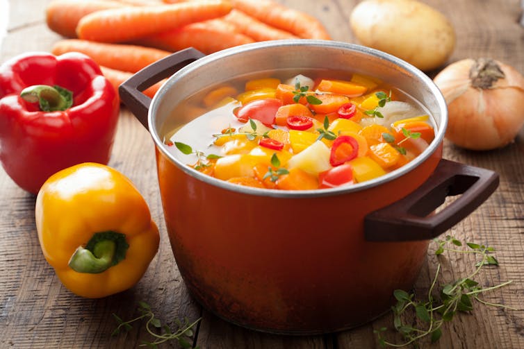 A pot full of stew with vegetables nearby.