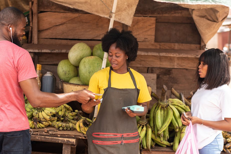 A woman wearing an apron and attending to a man and another woman in the market place.