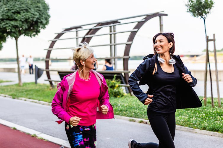 Two middle-aged women smile at each other while on a jog.