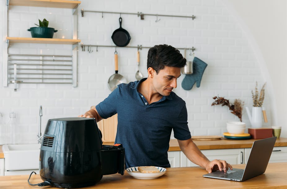 Man uses a laptop and air fryer in a modern kitchen