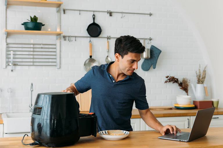 Man uses a laptop and air fryer in a modern kitchen