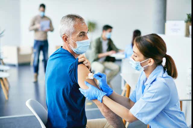 A nurse affixes a bandaid to a man's upper arm.