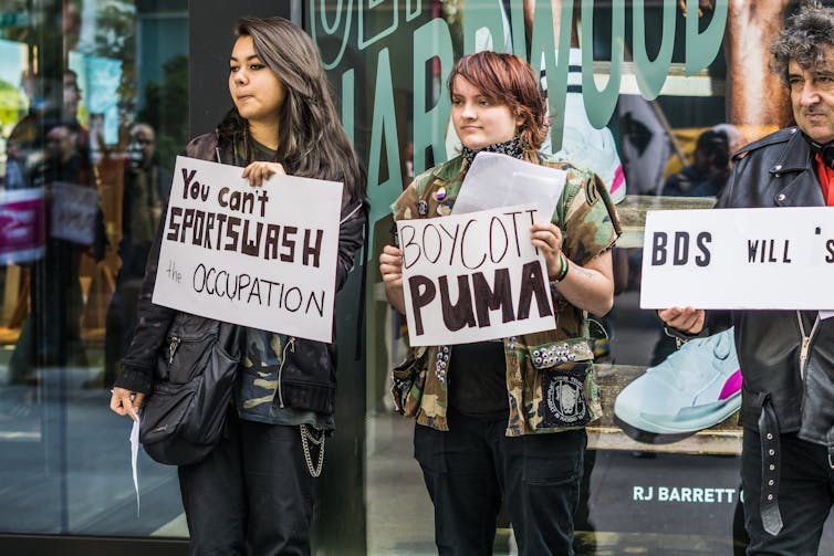 People stand holding signs that read: you can't sportwash occupation and boycott Puma.