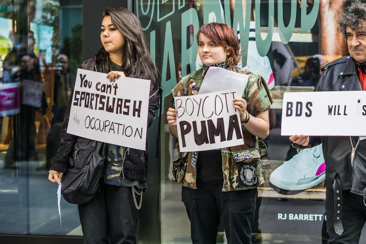 People stand holding signs that read: you can't sportwash occupation and boycott Puma.
