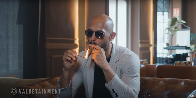 A man wearing sunglasses lights a cigar.