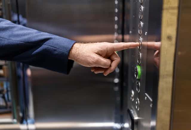 A man's hand reaches out to push a floor button in an elevator.