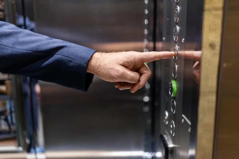 A man's hand reaches out to push a floor button in an elevator.