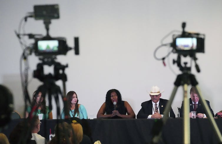 Five people sitting at a table looking out at tv cameras.