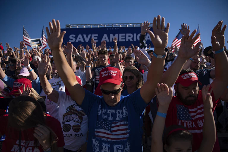 Personnes en tshirts et casquettes en l'honneur de Trump en train de prier pendant un meeting électoral