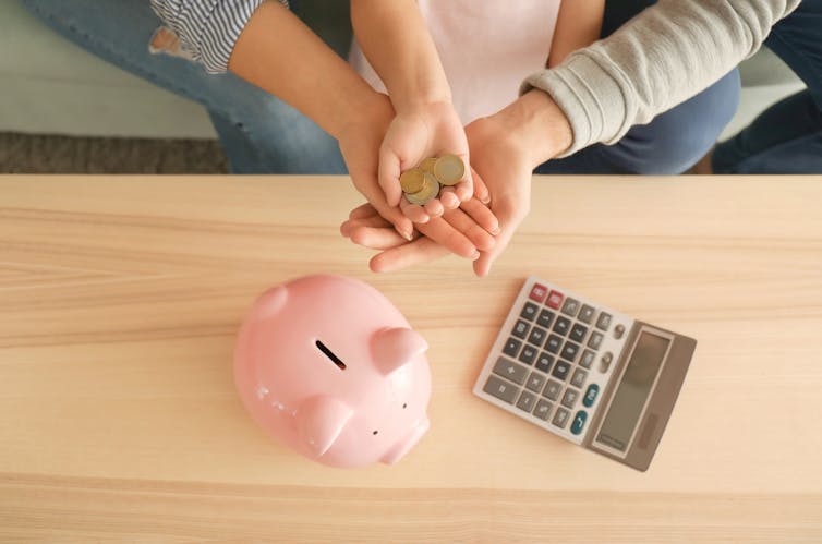 Overhead shot of three hands holding coins, calculator and piggy bank.