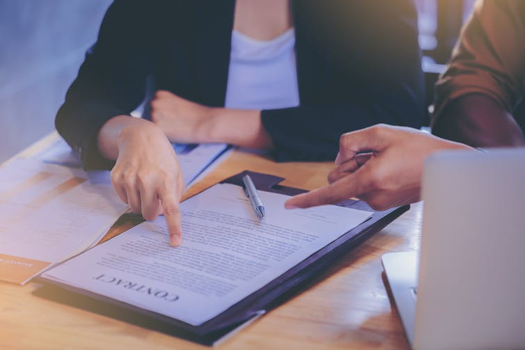Two people are discussing a contract and pointing to it on a desk in front of them.