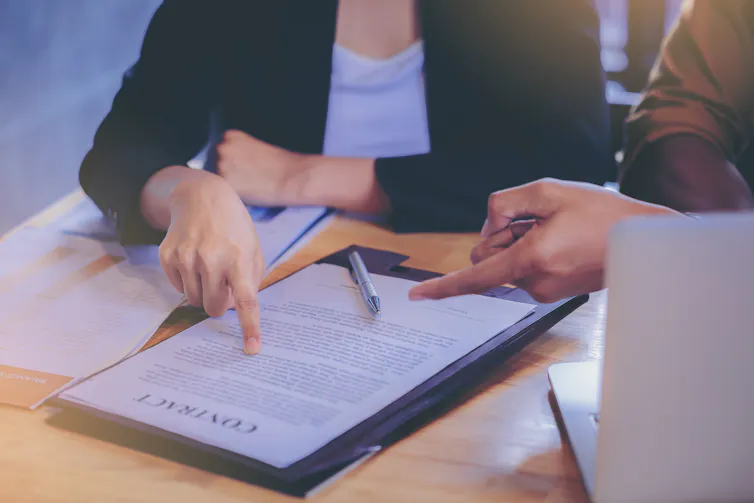 Two people in discussions about and pointing at a contract on a desk in front of them.