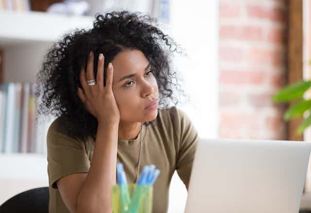 A tired woman sitting in front of a laptop, resting her head on her hand