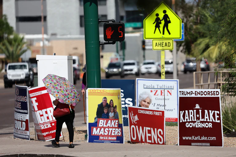 Woman holding an umbrella strolls past a series of campaign signs.