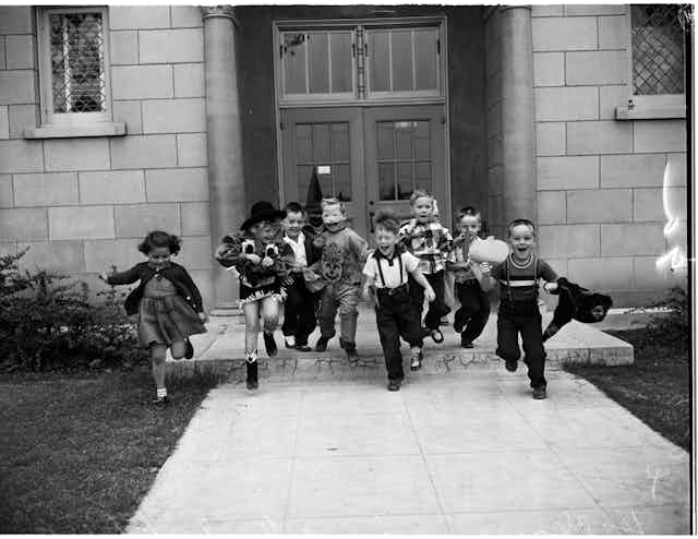 black and white photo of schoolchildren in halloween costumes running out the front door of school