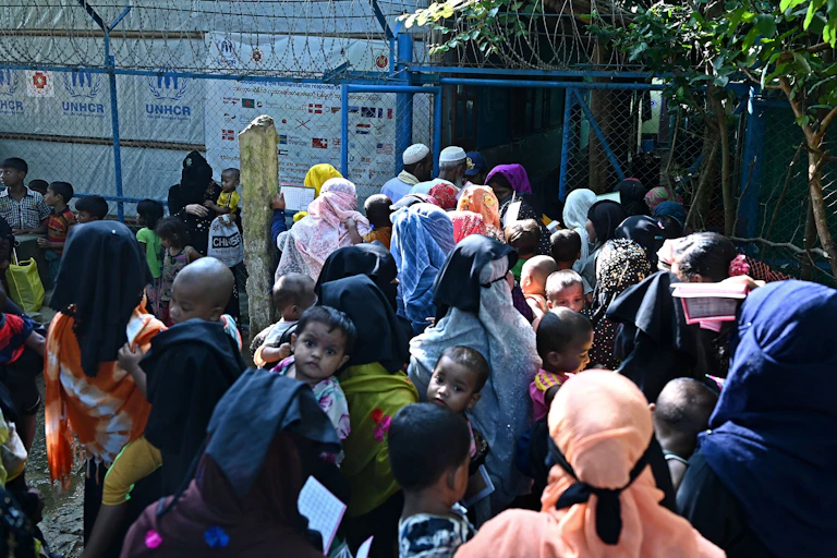 A crowd of people wearing religious head coverings stand near a barbed wire fence to collect relief supplies.