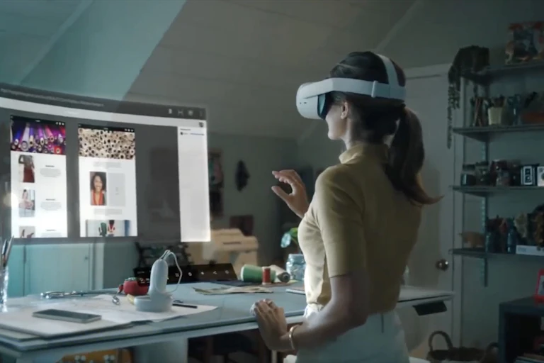 A photo of a woman wearing a VR headset looking at a virtual computer monitor floating above a desk.