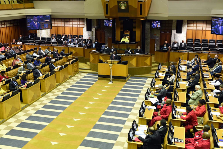 A man standing behind a podium addresses MPs seated to his left and right.