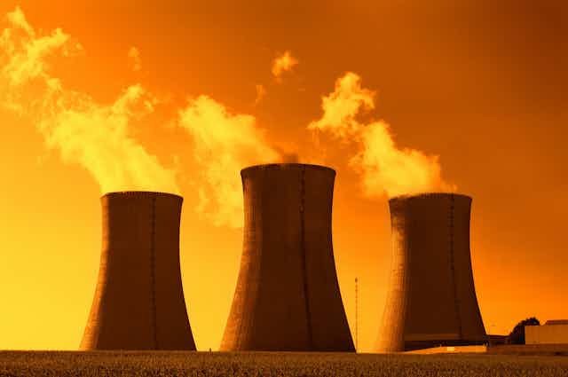 Torres de una central nuclear expulsando vapor bajo un cielo rojizo.