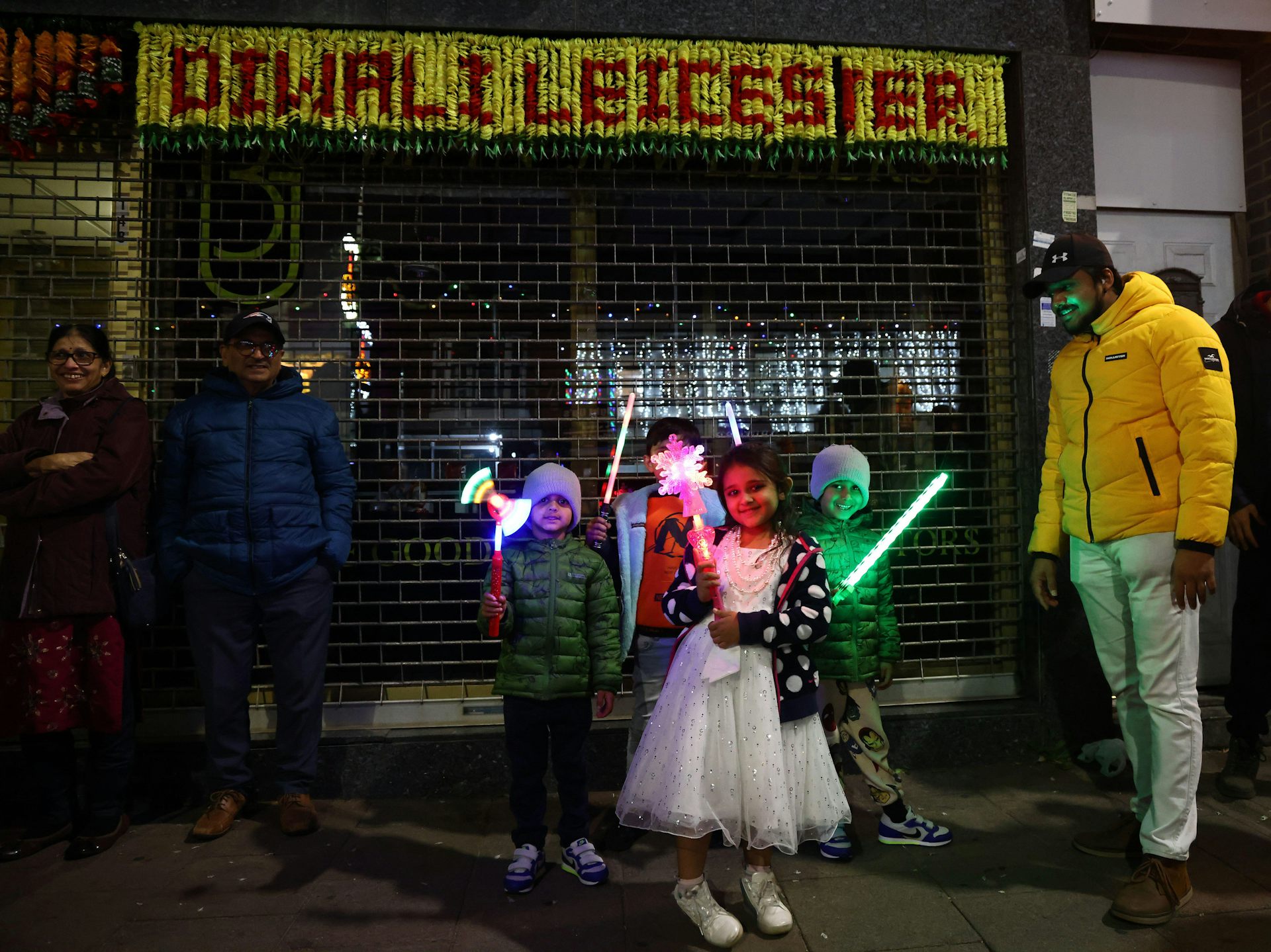 Children in fancy dress with lit-up toys on a pavement at night.