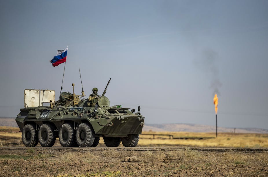 Véhicule blindé surmonté d'un drapeau russe devant un champ de pétrole en Syrie