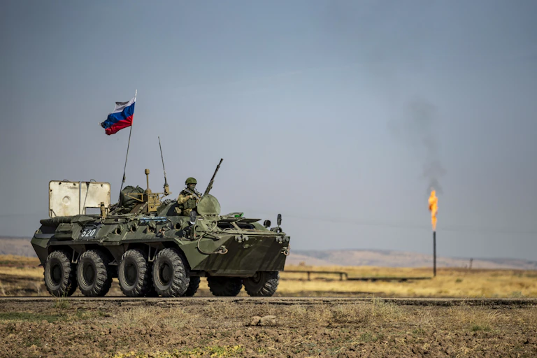 Véhicule blindé surmonté d'un drapeau russe devant un champ de pétrole en Syrie