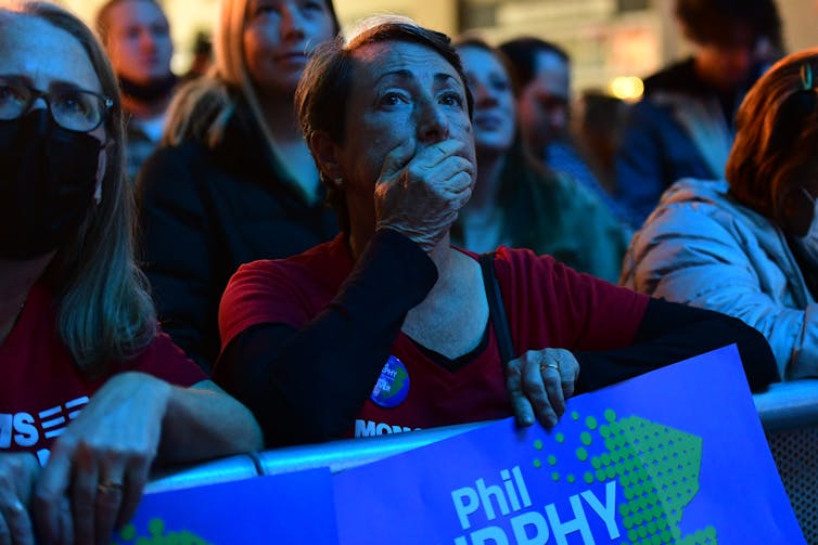 A shocked looking woman in a crowd, with her hand over her mouth.