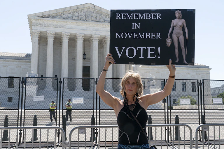 A woman holds a sign with an image depicting Medusa that says, "Remember in November, Vote!," outside of the Supreme Court in Washington.