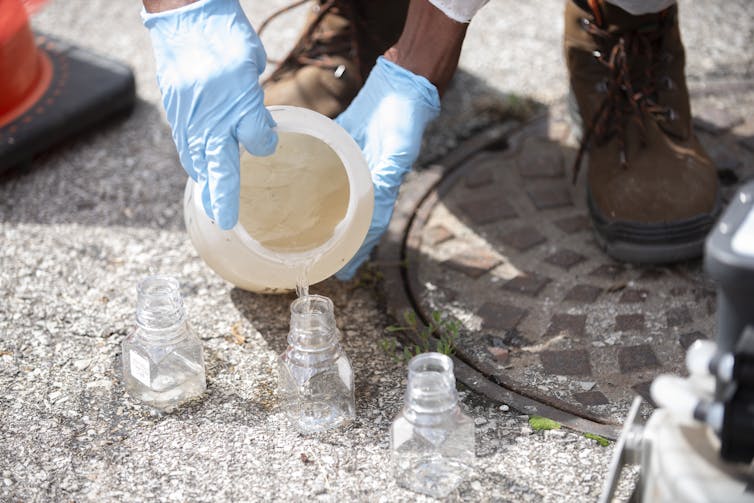 Man in protective gear pouring wastewater sample into a clear jar