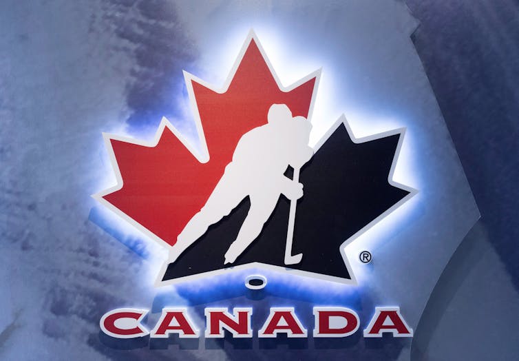 A photo of the Hockey Canada logo: A black and red maple leaf with an outline of a hockey player hockey with the word Canada below.