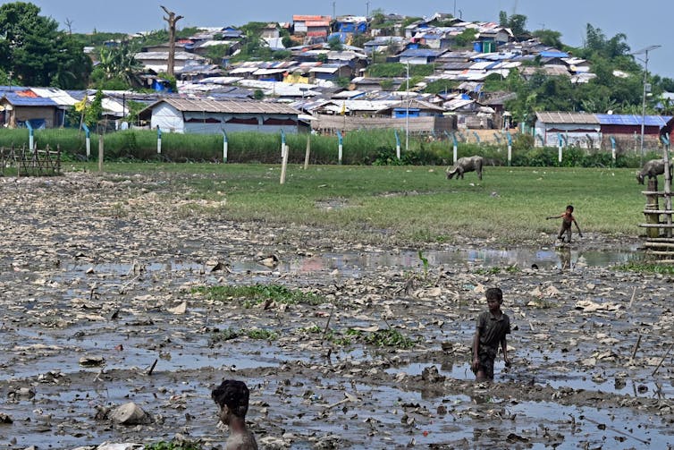 Three children are walking in garbage and mud.