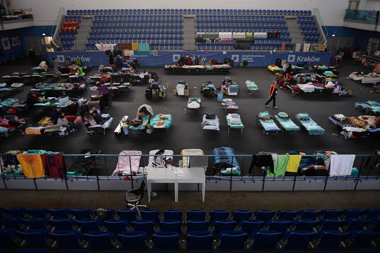 Dozens of sleeping cots are seen on the middle of a gymnasium floor.