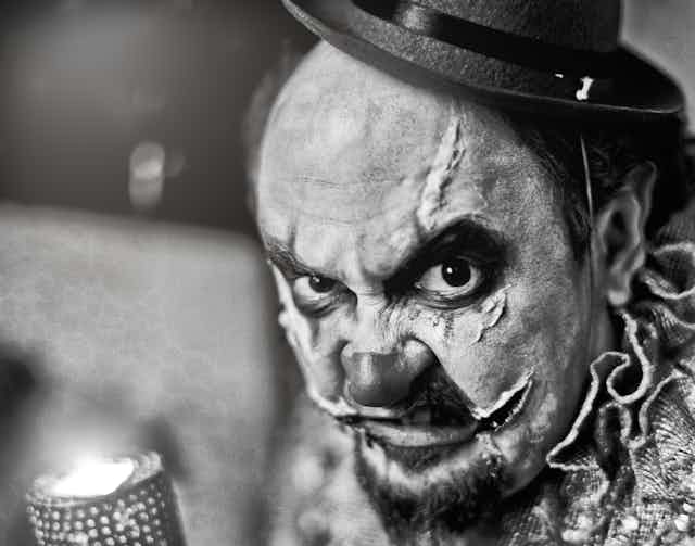 Black and white photo of snarling clown with scars.