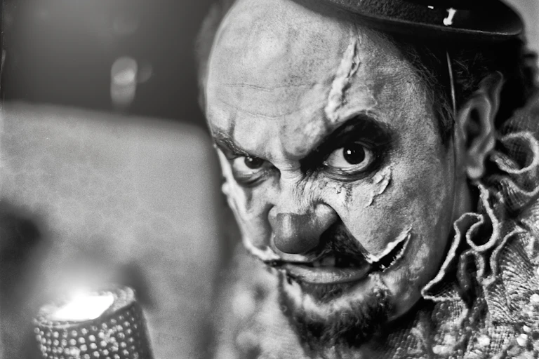 Black and white photo of snarling clown with scars.