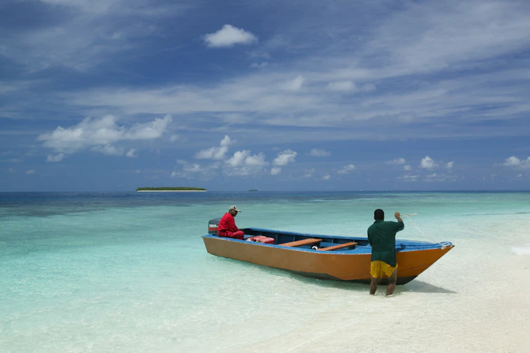 Two men in a fishing boat on a sandy beach in Tuvalu with islands in the background.