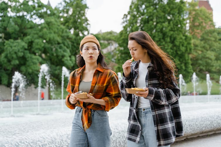 Two people walk and chat while eating.
