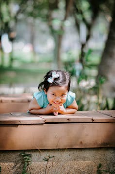 A happy child, learning on a wooden deck.