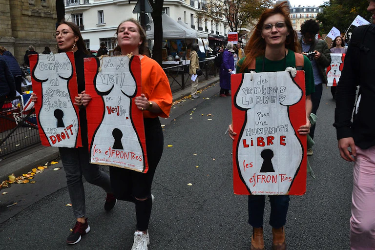 Trois femmes portent des panneaux représentant des corps de femmes inscrits de mentions pour le droit à disposer de leurs coprs