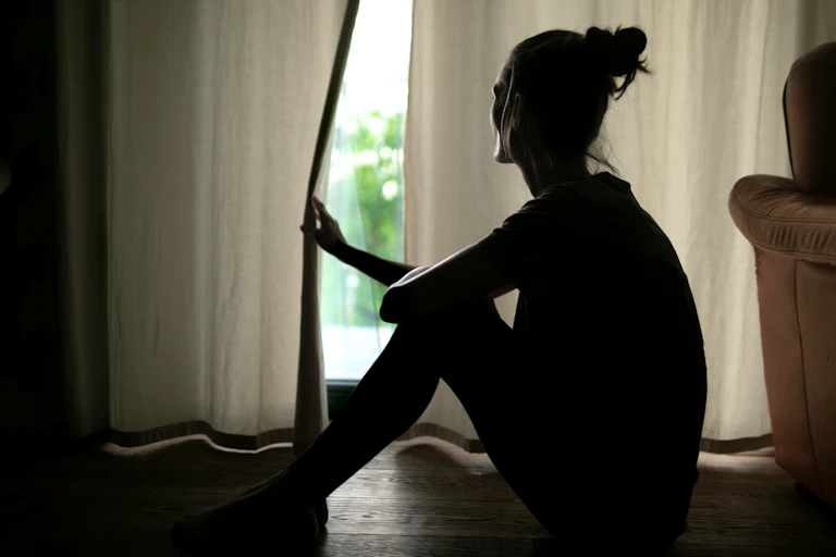 A woman in the shadows opens a curtain to look out