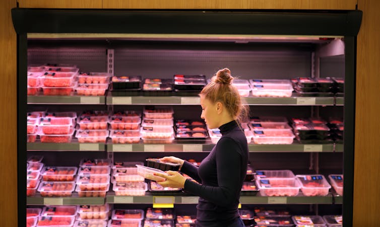 Een vrouw selecteert een pakje vlees uit de vleesafdeling van een supermarkt.
