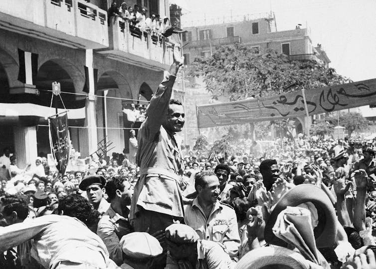 A black and white photo shows a man waving to a large crowd.